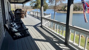 Un porche cubierto con bancos y mesas de madera, con vista a un lago con un muelle y árboles.