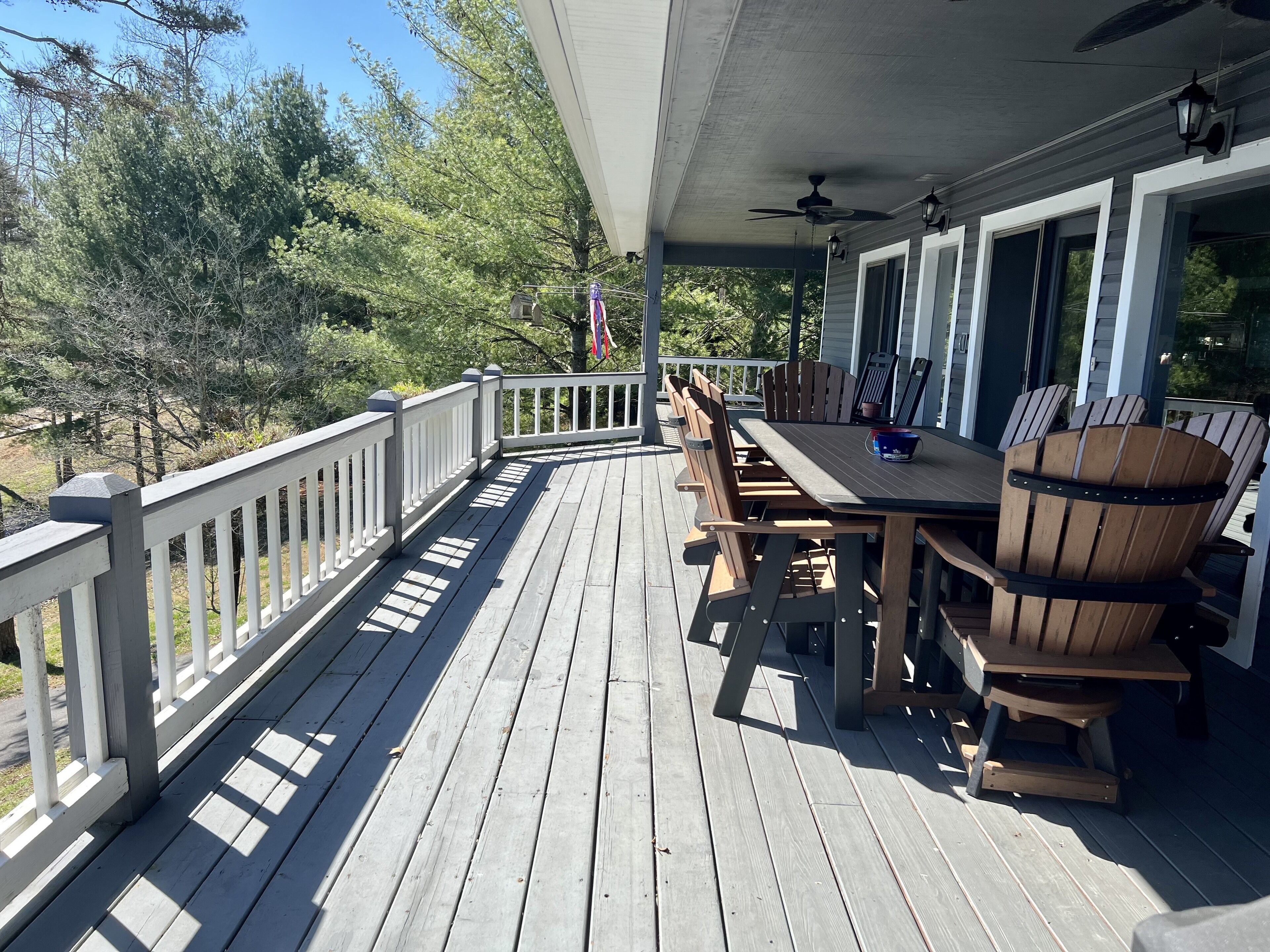 Een houten terras met een tafel, stoelen en een plafondventilator, met uitzicht op bomen.