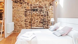 A bedroom with a stone wall, a bed with white bedding, a wooden headboard, and a hanging clothes rack. - A Forxa - Casa Ferrador (Ribeira Sacra) (Bolmente)