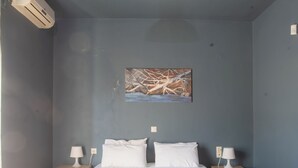 Une chambre à coucher comprenant un lit, deux tables de chevet, une lampe fixée au mur, un climatiseur et un tableau.