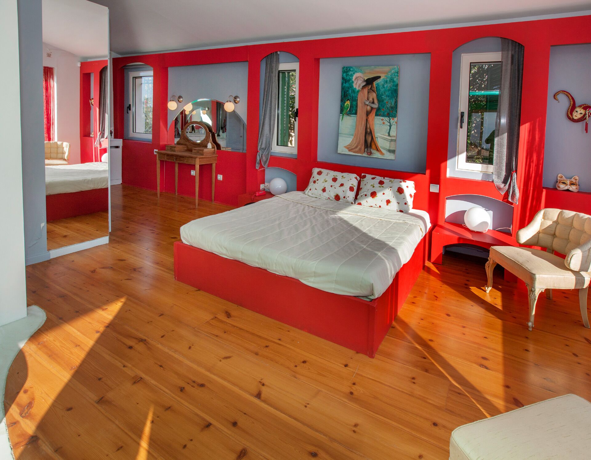 Une chambre spacieuse avec un grand lit, une coiffeuse avec un miroir et un tableau accroché au mur.