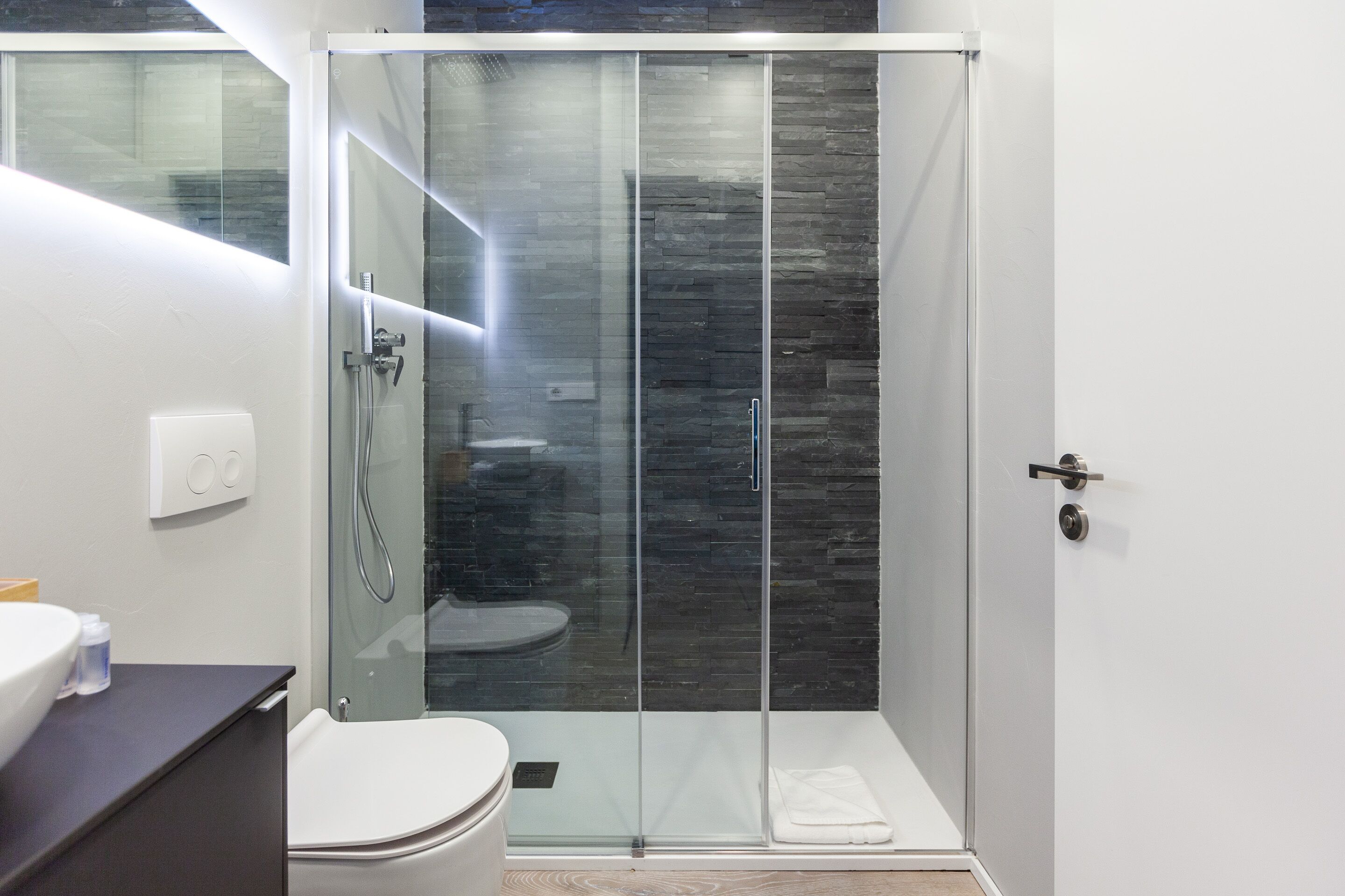 A modern bathroom with a glass-enclosed shower, a white toilet, and a dark wooden vanity.