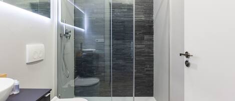 A modern bathroom with a glass-enclosed shower, a white toilet, and a dark wooden vanity.