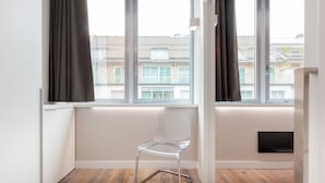 A room with a clear view of the outside through large windows, a white chair, and a wooden floor. - easyhomes - City Centre Suites (Milan)