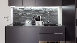 A modern kitchen with dark cabinets, a stone backsplash, and a built-in coffee maker. - easyhomes - City Centre Suites (Milan)