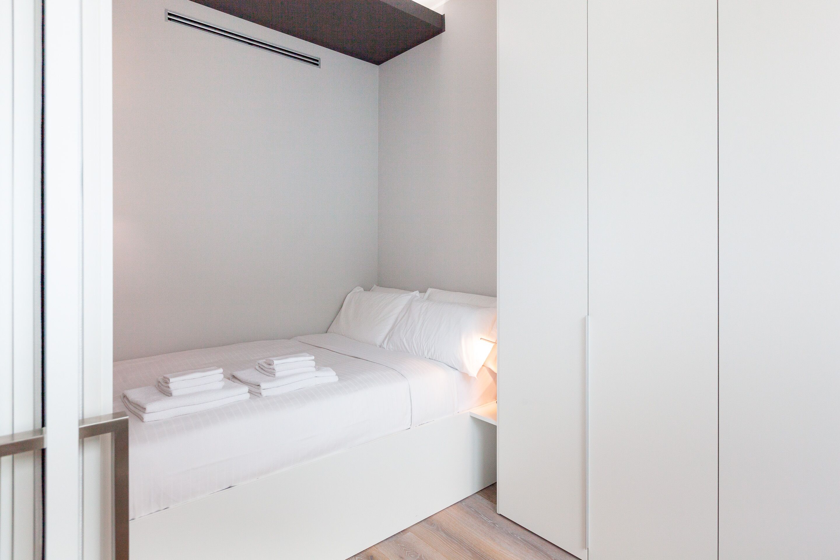 A minimalist bedroom with a bed, pillows, and neatly folded towels.