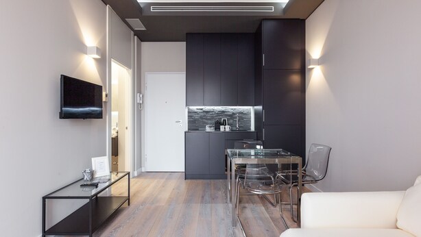 A modern kitchen with dark cabinetry, a glass dining table, and a white sofa. - easyhomes - City Centre Suites (Milan)