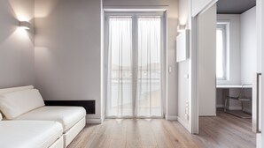 A modern, minimalist room with a white sofa, a wooden floor, and a sliding glass door leading to a balcony. - easyhomes - City Centre Suites (Milan)