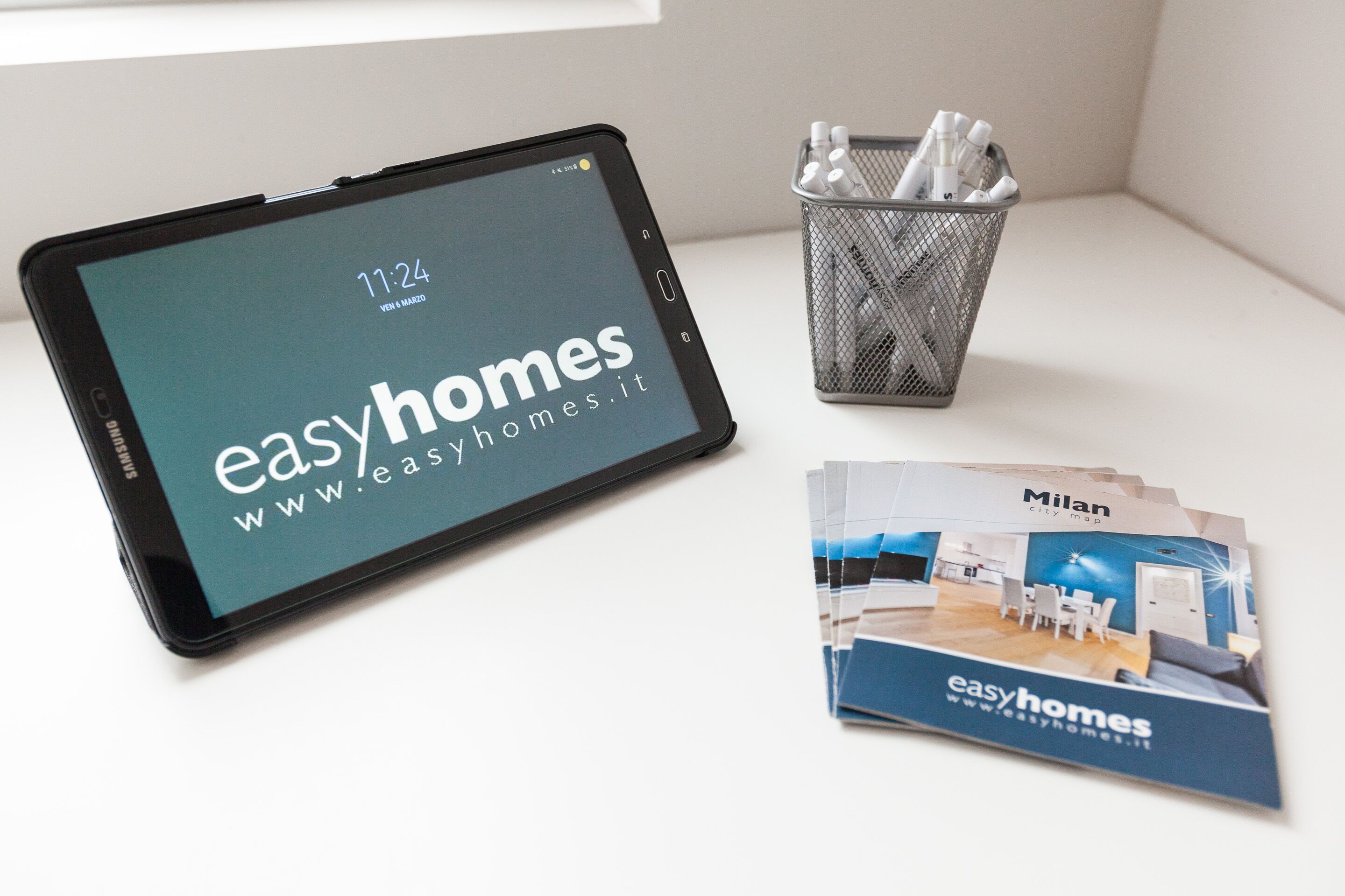 A tablet displaying the website 'www.easyhomes.it', a metal basket with pens and markers, and brochures for 'easyhomes'.