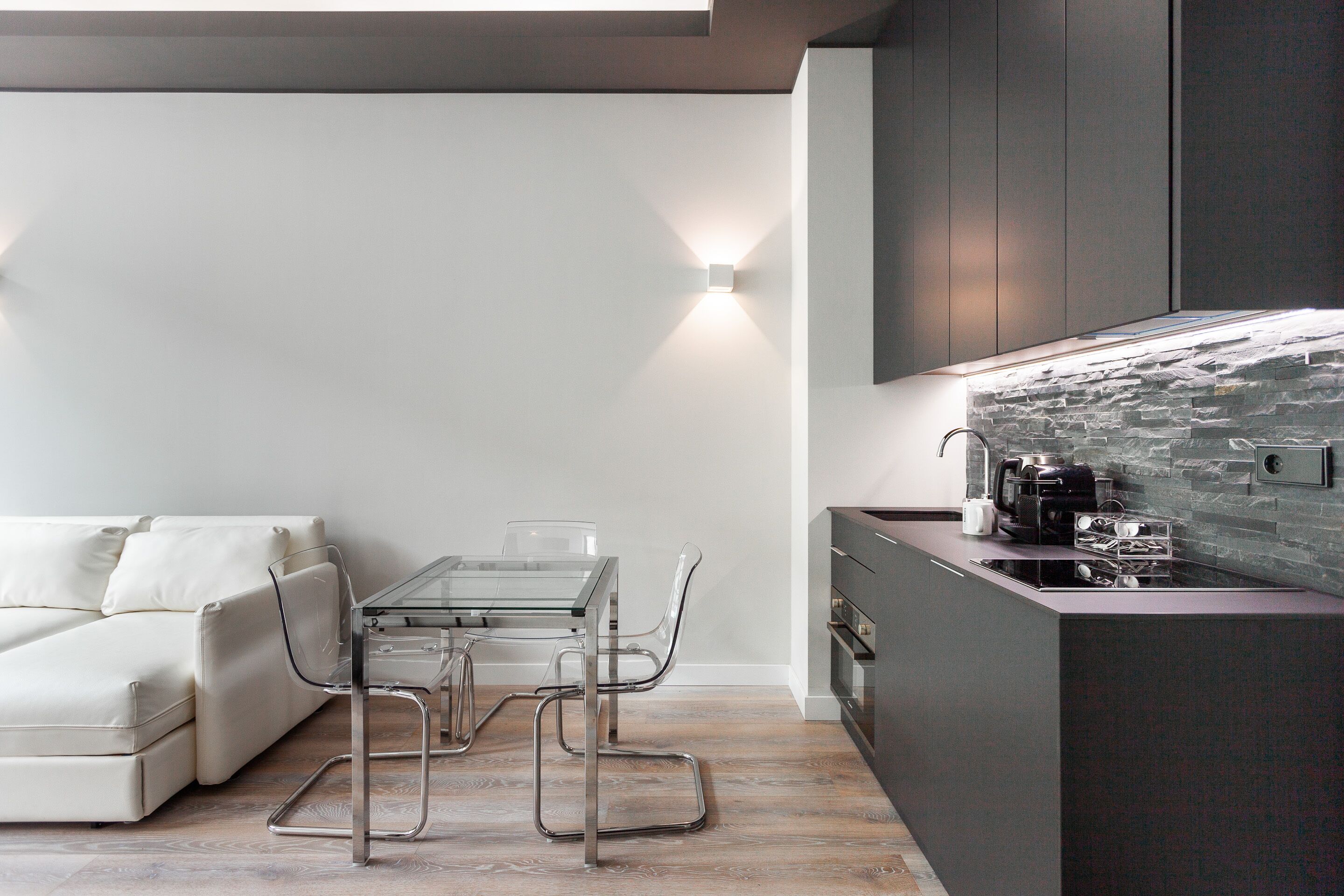Una cocina moderna con protector contra salpicaduras de piedra, una mesa de comedor de vidrio y un sofá blanco.