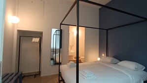 A four-poster bed with white linens, a bedside table with a lamp, and a mirror on the wall. - easyhomes - City Centre Suites (Milan)