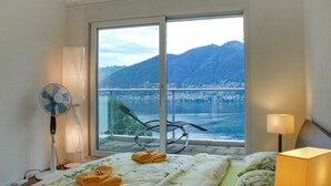 Une chambre d’hôtel avec un lit, un ventilateur, une lampe et une vue sur un lac et des montagnes.