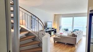 Un salon moderne avec un escalier en colimaçon, un canapé, un téléviseur et une vue sur la mer.