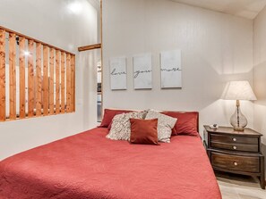 A bedroom with a bed, pillows, a nightstand, a lamp, and wall art.