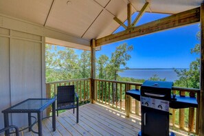 A covered outdoor area with a grill, a table, and a chair, overlooking a body of water.