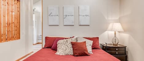 A bedroom with a large bed, a nightstand, a lamp, and three wall-mounted signs with text.