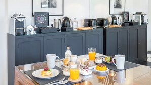 Een ontbijtbuffet met diverse gerechten en drankjes, een koffieapparaat en een lijst in een fotolijst aan de muur.