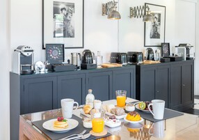 Um buffet de café da manhã com diversos alimentos e bebidas, uma máquina de café e um quadro na parede.