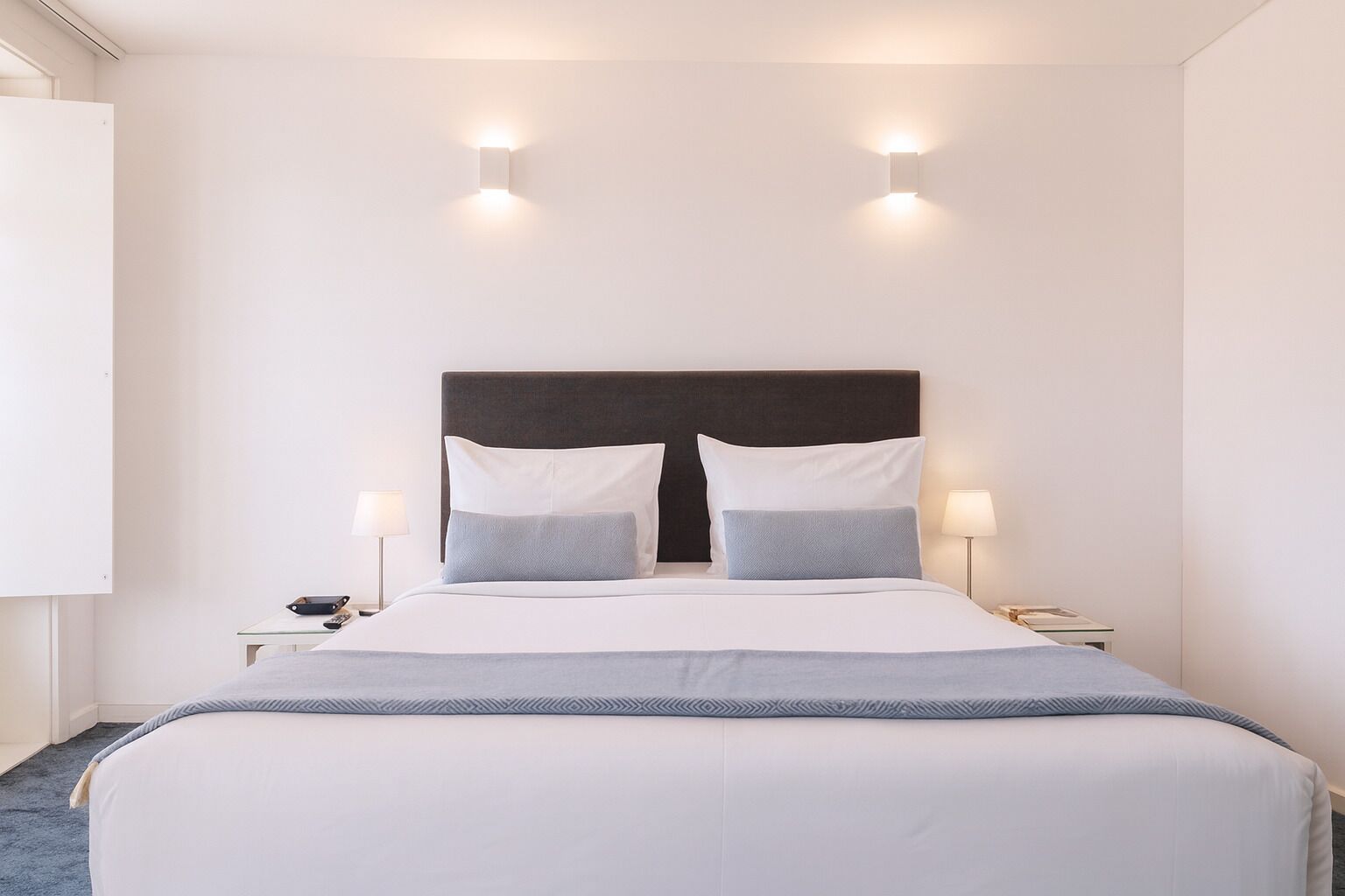 A hotel room with a large bed, two bedside tables, and wall-mounted lighting.