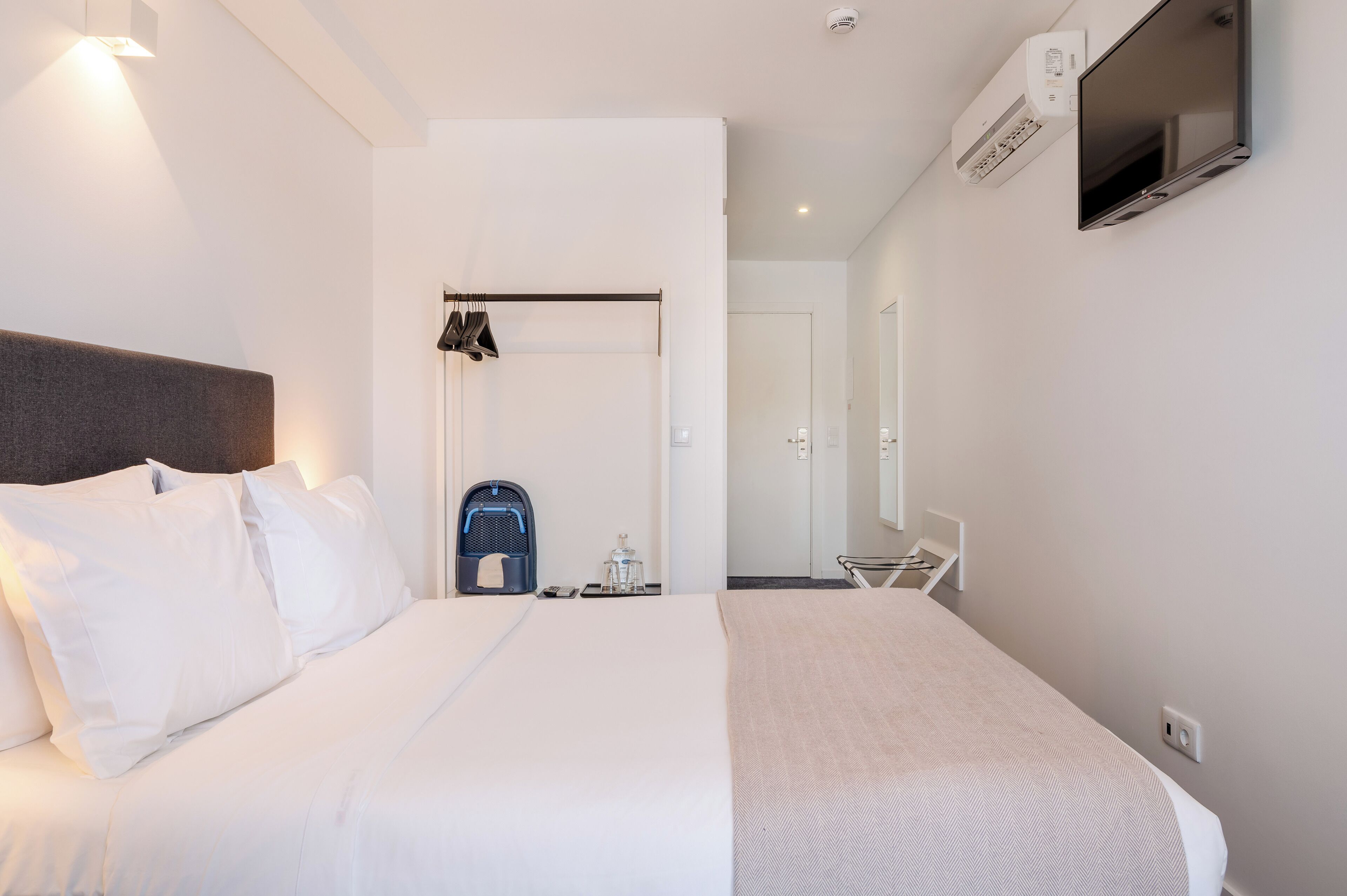 A modern hotel room with a large bed, a TV mounted on the wall, and a ceiling-mounted air conditioning unit.