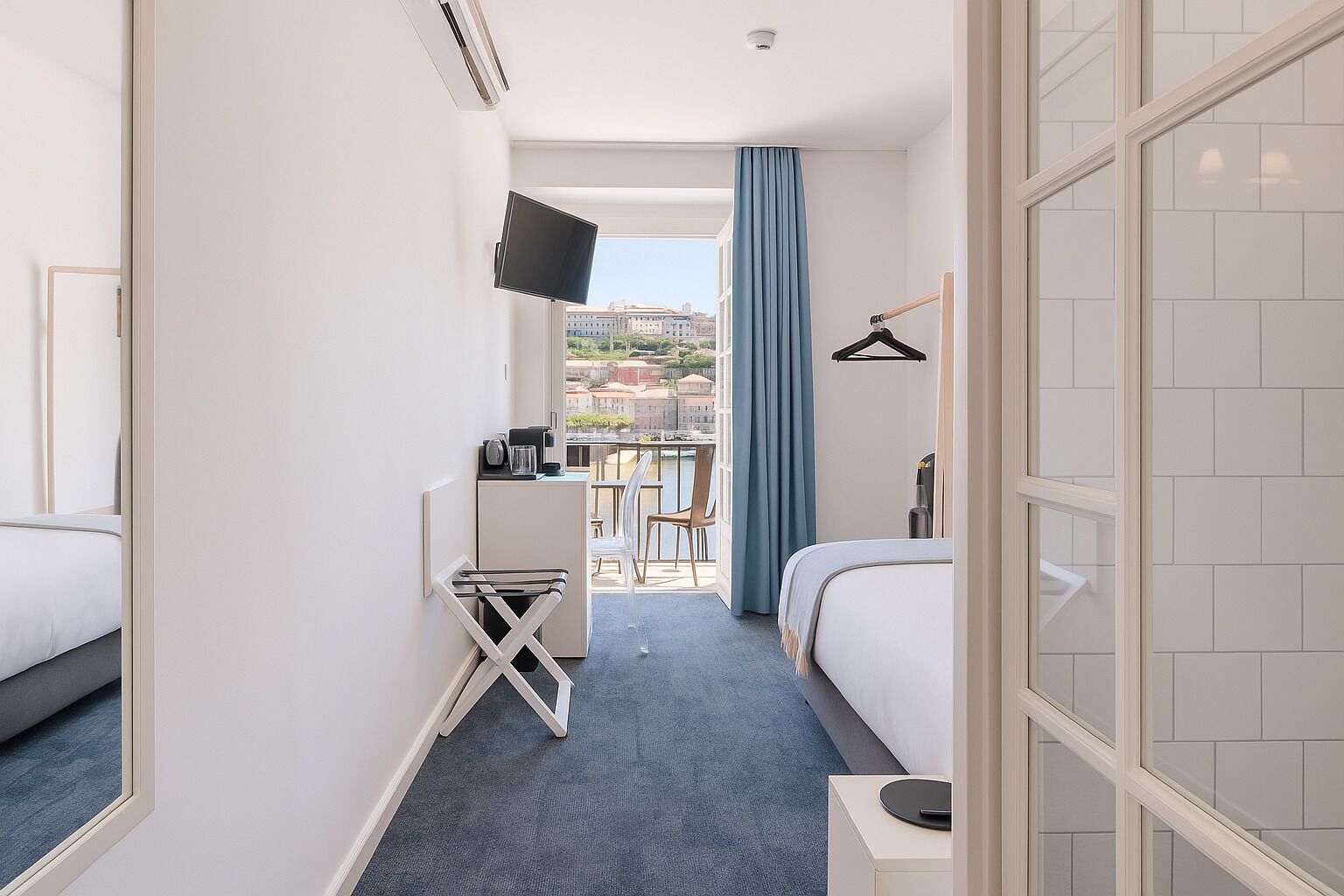 Habitación de hotel con dos camas, un escritorio, una silla, televisión y balcón con vista a edificios.