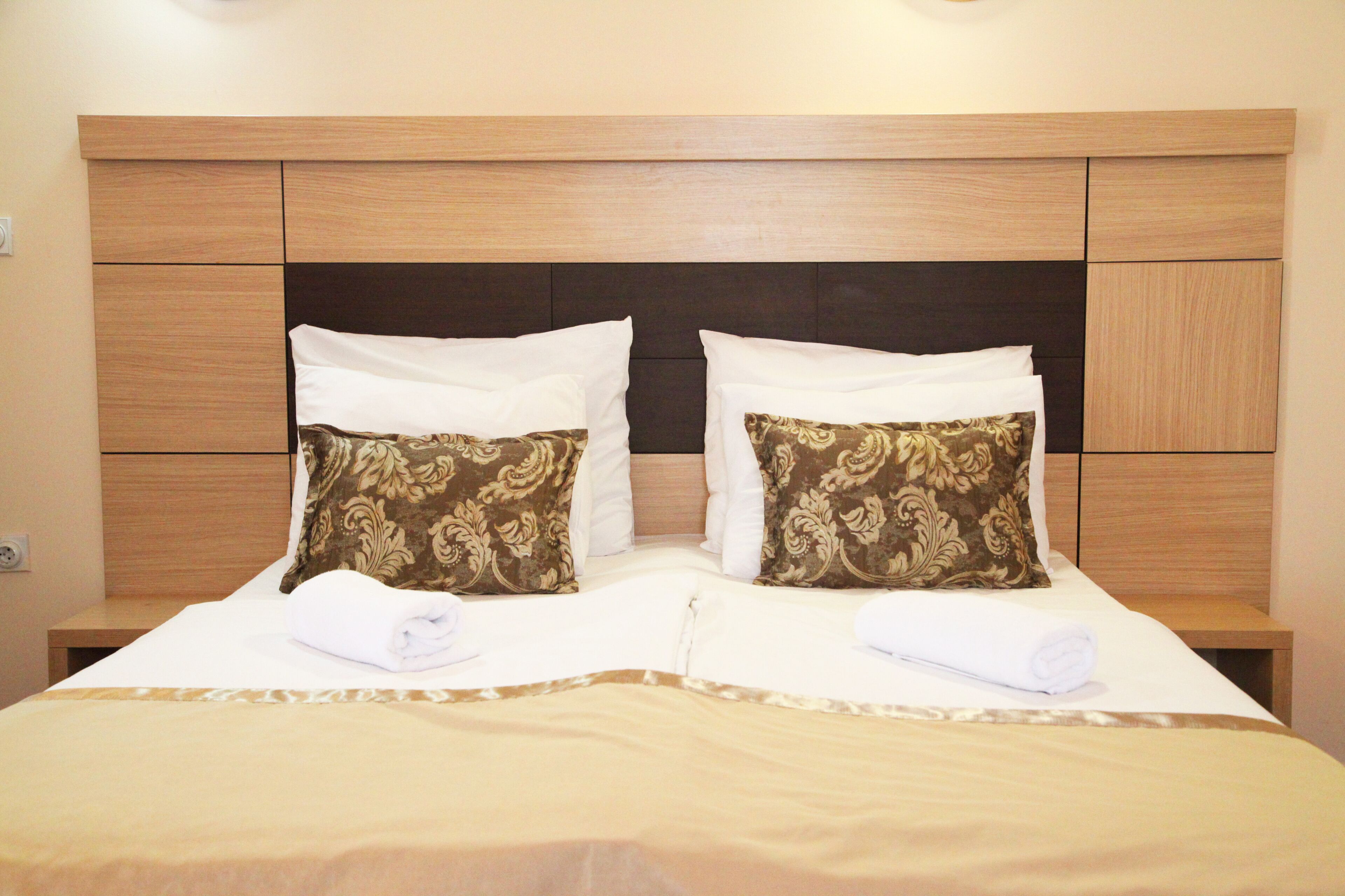 A double bed with a wooden headboard, two decorative pillows, and a neatly folded white towel.