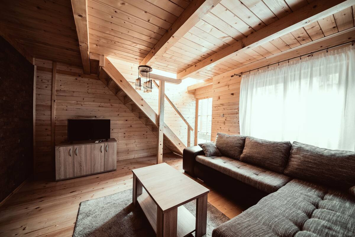 Interior em madeira com sofá, televisão e escada.