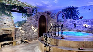 Una habitación con paredes de piedra, una chimenea, una piscina y una escalera que lleva a un balcón.