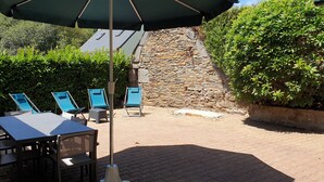 Un patio al aire libre con una mesa y sillas, un muro de piedra y abundante vegetación.