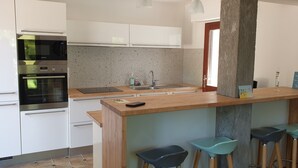 Una cocina moderna con armarios blancos, horno de acero inoxidable, encimera de granito, un lavamanos y una zona de bar con taburetes.