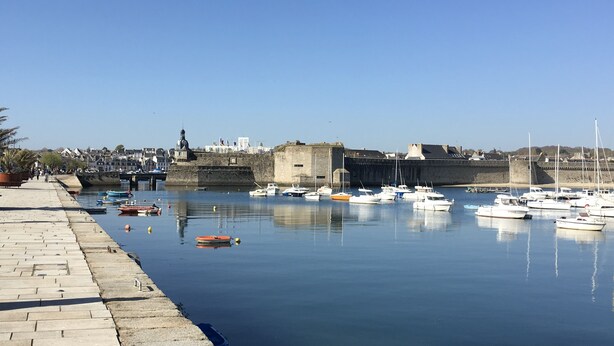 Un puerto con barcos amarrados, un muro de piedra y cielo despejado.