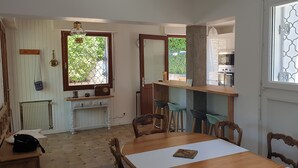 Un comedor con una mesa y sillas de madera, una zona de cocina con estufa y mostrador, y una ventana con mosquitero.