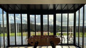 A room with a foosball table and a view of a green landscape through large windows. - Villa l'Etable, 4 bedrooms (Trouville-sur-Mer)