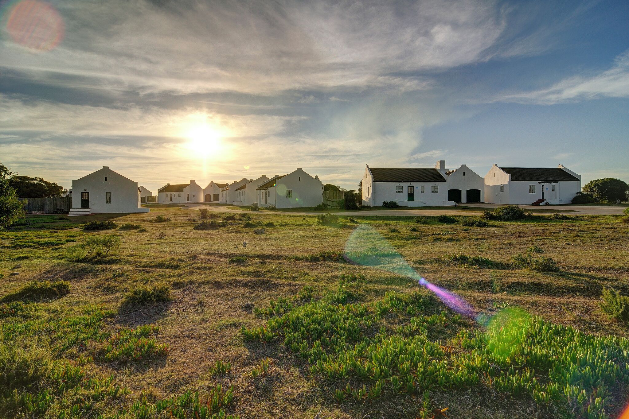 A row of white buildings with a grassy field in front, under a clear sky.