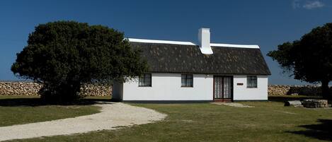 A white house with a black roof, a chimney, and a stone wall in the background.