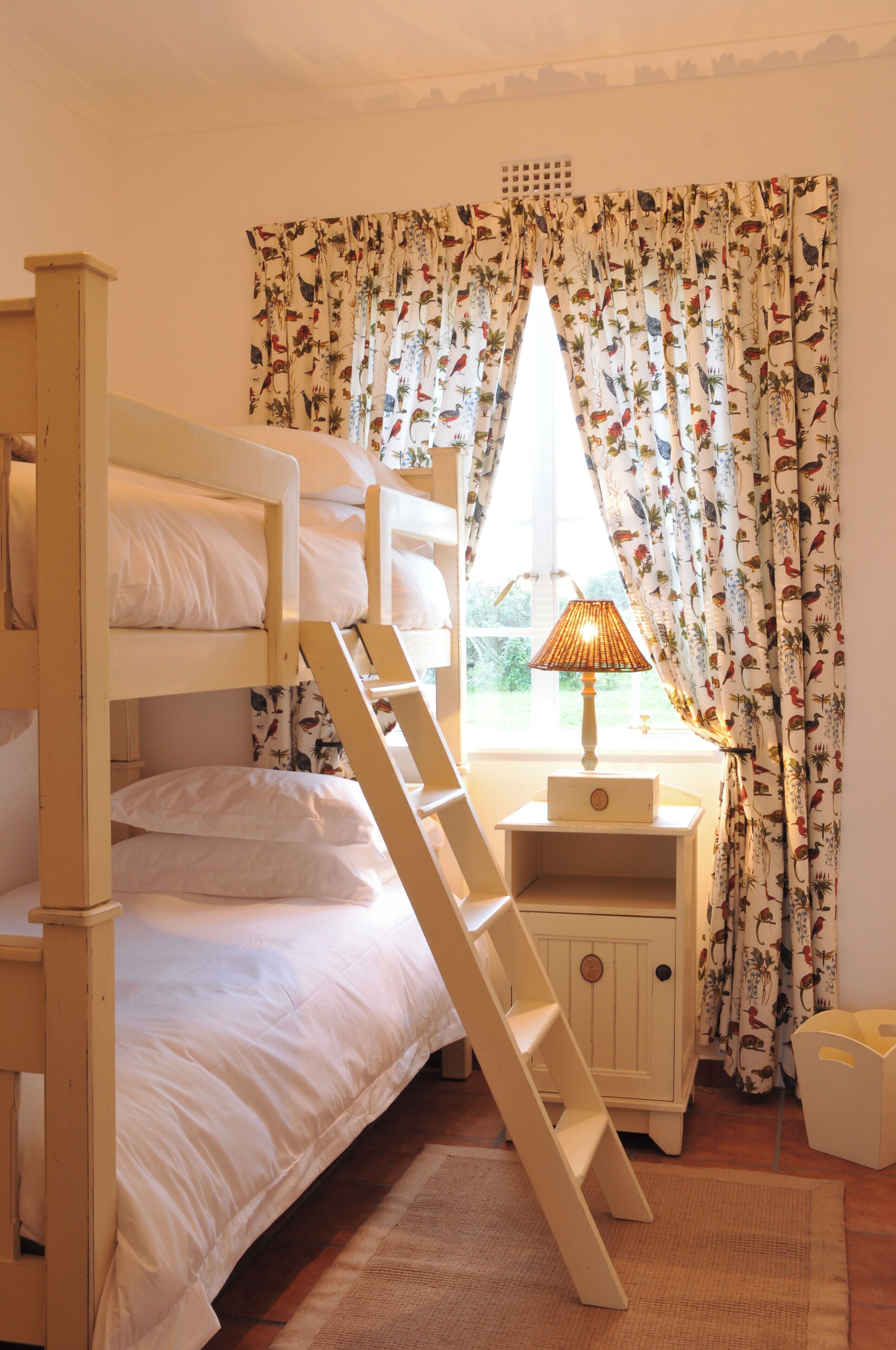 A bunk bed with a wooden ladder, a bedside table with a lamp, and floral curtains.