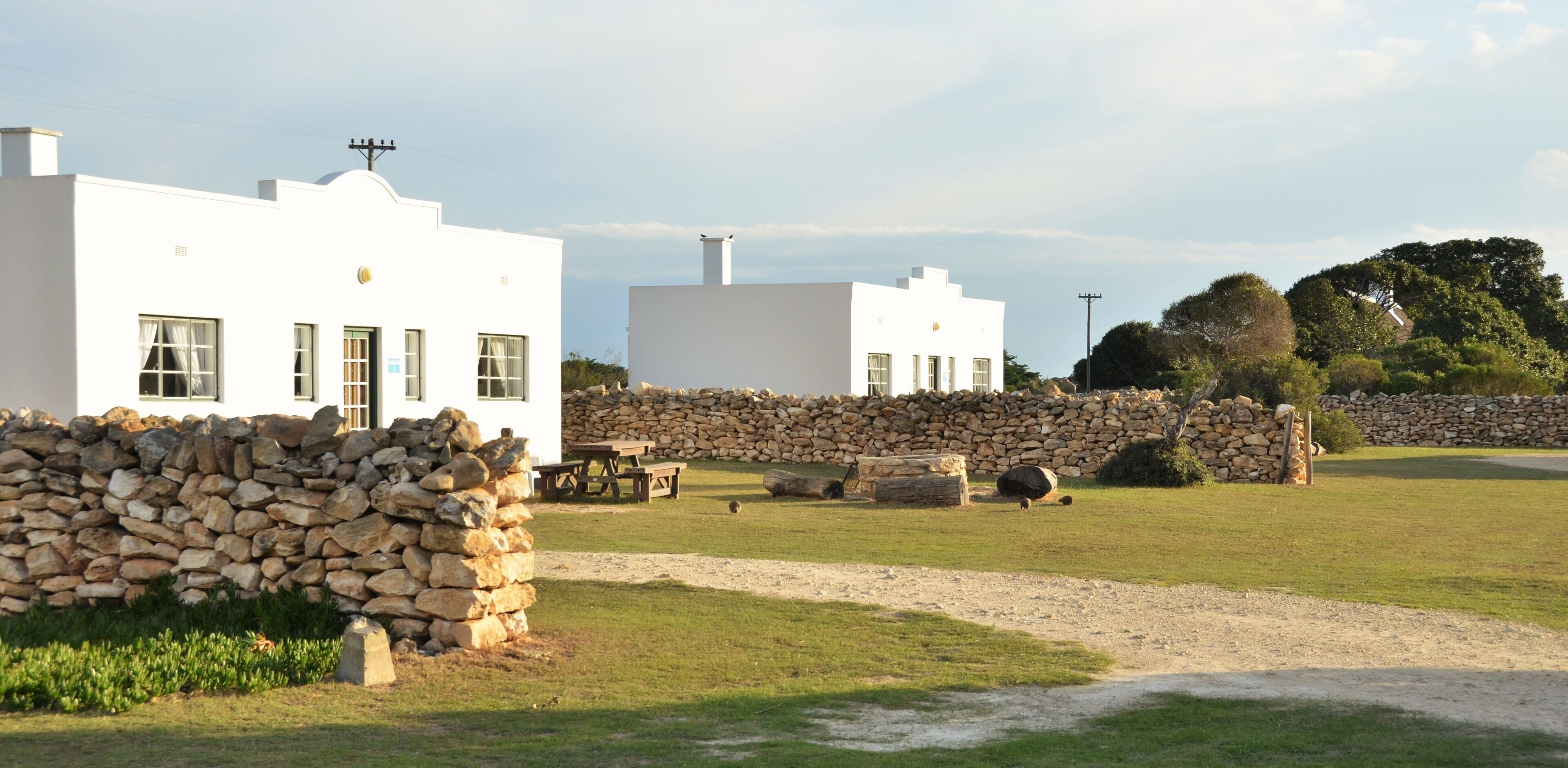 A white building with a stone wall and a grassy area in front.