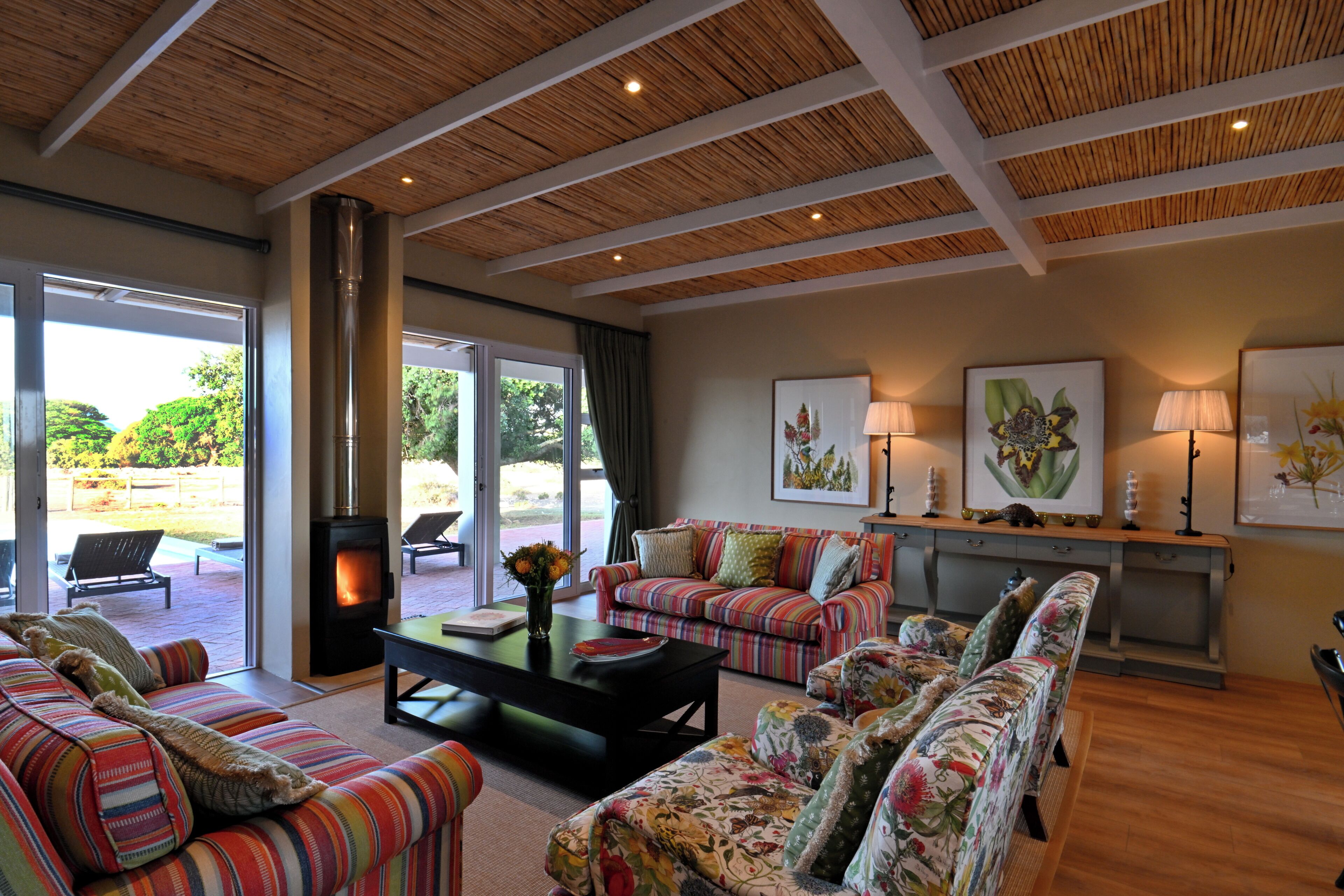 A spacious living room with a large sofa, a smaller sofa, a coffee table, and a fireplace. There are two lamps on a console table and a large window providing a view of the outdoors.