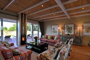 Un salon spacieux comprenant un grand canapé, un canapé plus petit, une table basse et une cheminée. Une console porte deux lampes, et une grande fenêtre offre une vue sur l’extérieur.