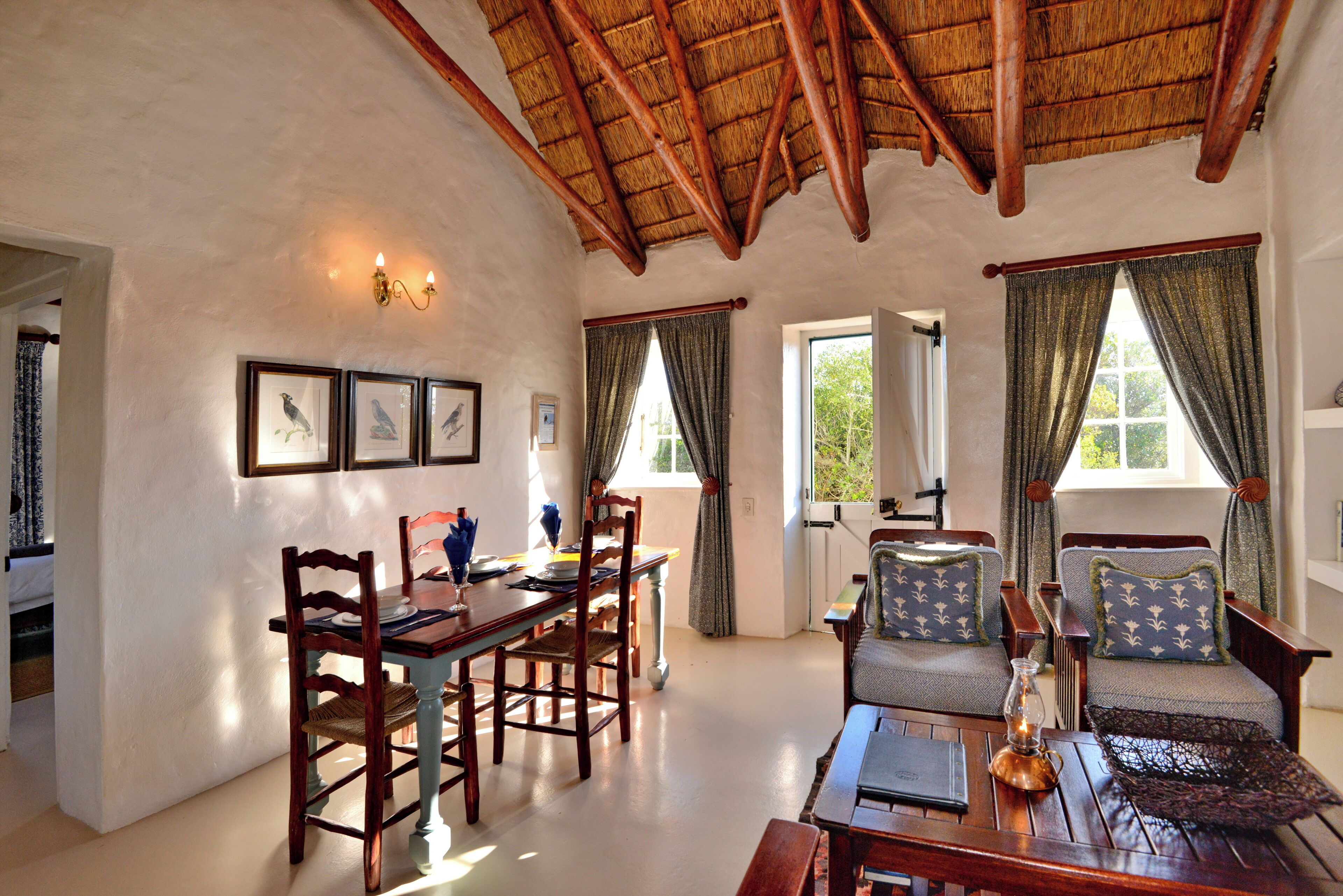 A spacious room with a high ceiling, a dining area with wooden furniture, and a cozy seating area with patterned cushions.