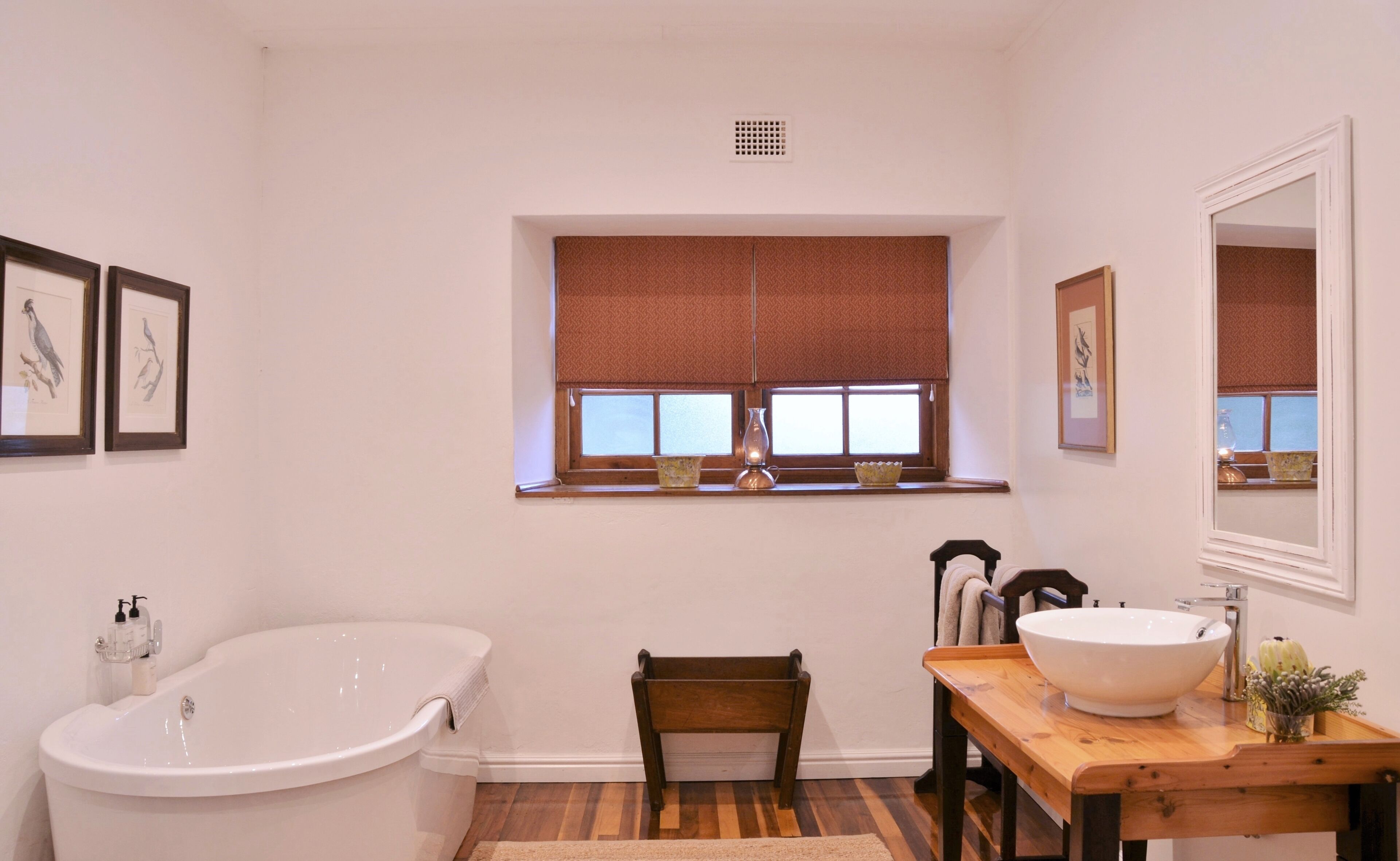 Ein Badezimmer mit einer freistehenden Badewanne, einem Holzstuhl, einem Waschbecken und einem Fenster mit Jalousien.