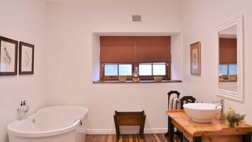 Ein Badezimmer mit einer freistehenden Badewanne, einem Holzstuhl, einem Waschbecken und einem Fenster mit Jalousien.