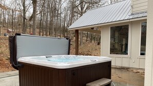 A hot tub with a wooden exterior, a step for access, and a metal roof structure in the background.