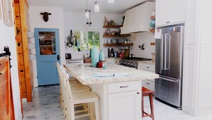 A kitchen with a central island, wooden chairs, a stainless steel refrigerator, and a blue door.