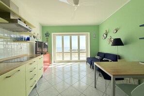 A room with a kitchen, dining area, and a large sliding glass door leading to a balcony.