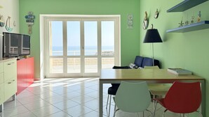 A room with a large sliding glass door leading to a balcony, a dining table with chairs, a TV on a cabinet, and shelves with decorative items. - N226 - Numana, wonderful two-room apartment facing the sea (Numana)