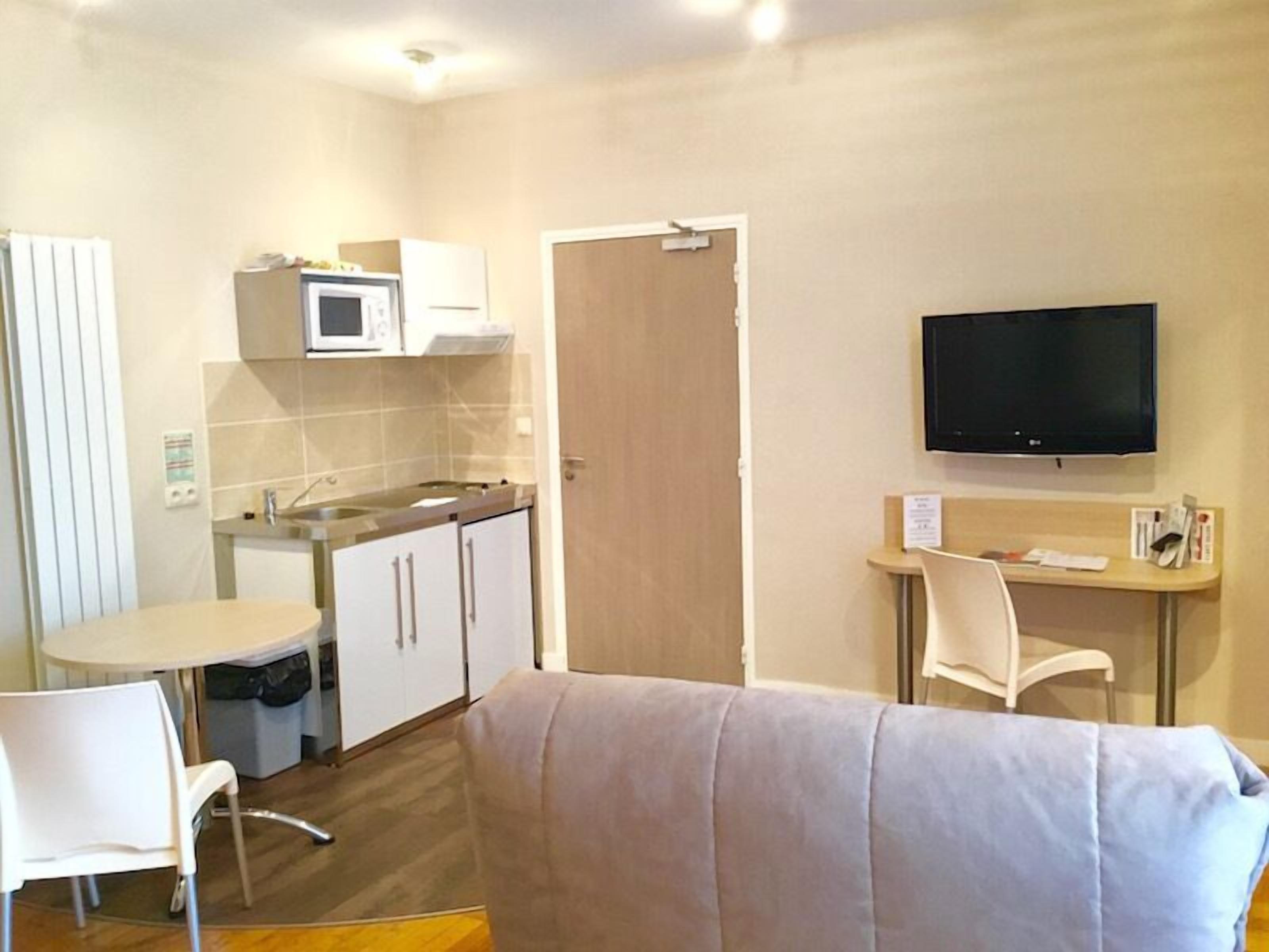 Una habitación de hotel compacta con kitchenette, televisión, cama y una pequeña mesa.