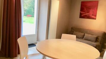 A room with a round table and chairs, a sofa, a window with curtains, and a red abstract painting on the wall.