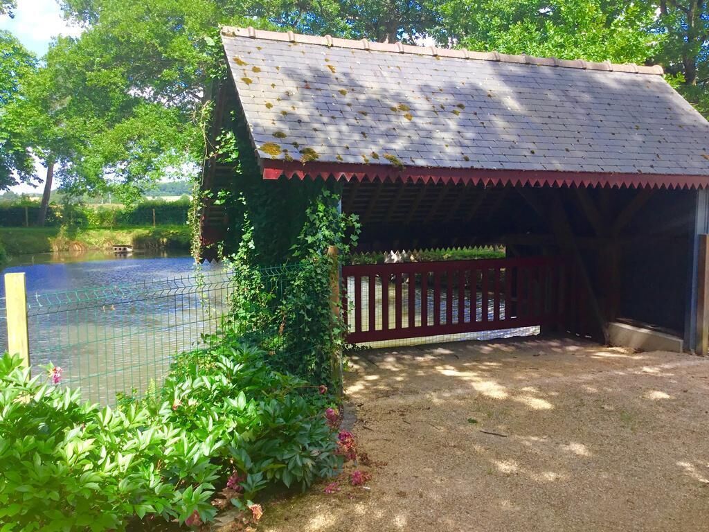 A covered outdoor area with a wooden fence, a pond, and greenery.