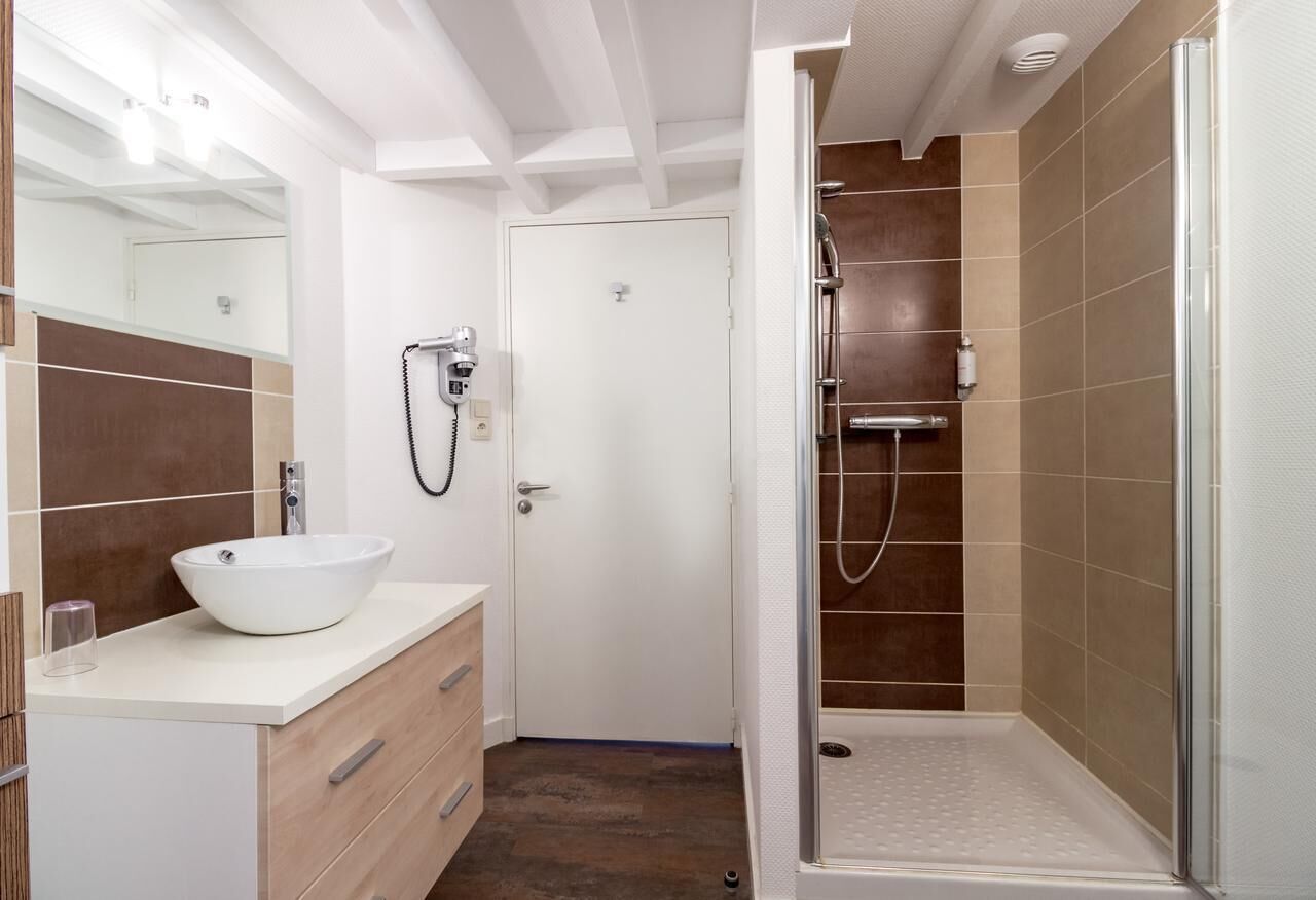 A modern bathroom with a white sink, a glass shower enclosure, and a door leading to another room.